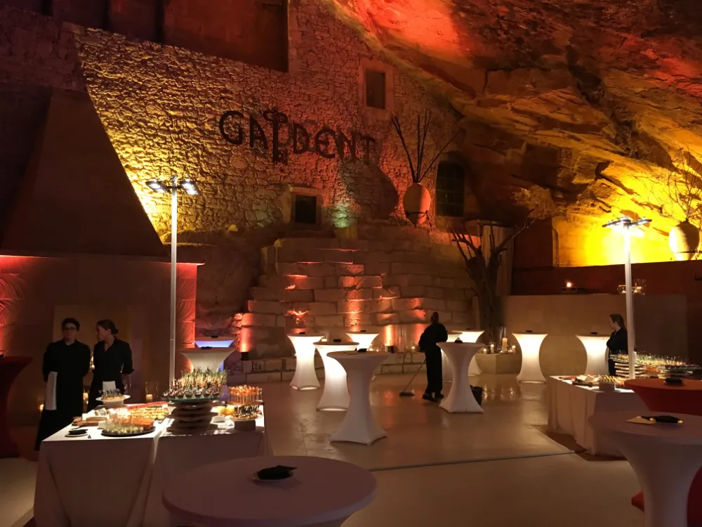 vent reception set up inside a cave-like venue with rough stone walls and warm lighting, featuring glowing white cocktail tables, buffet stations with appetizers, and waitstaff standing by